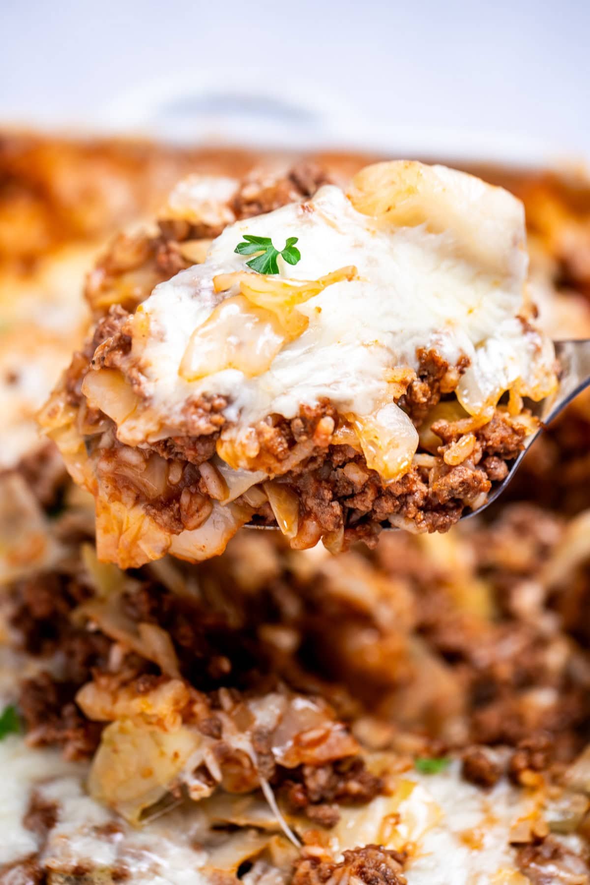 A spatula lifting some cabbage roll casserole out of a baking dish, topped with fresh parsley.