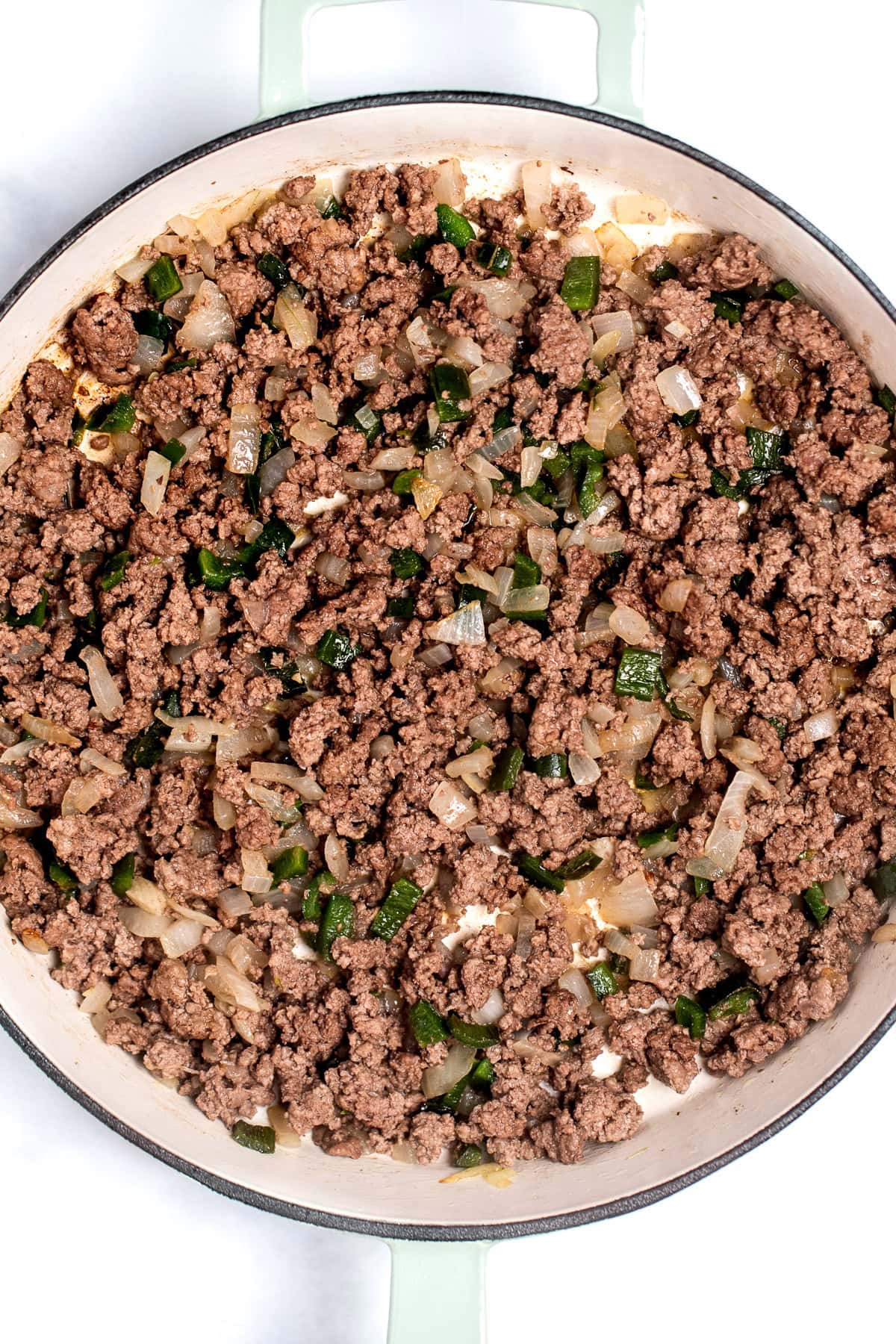A skillet with browned ground beef with peppers and onions.
