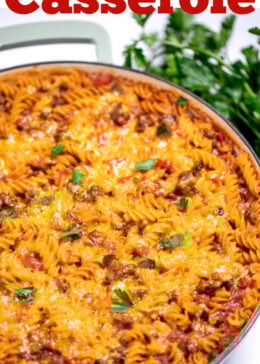Pinterest pin with a cheeseburger casserole skillet with ground beef, gluten free rotini pasta, peppers, and onion topped with cheddar cheese and broiled, then topped with fresh parsley. There's fresh parsley on the table next to the skillet.