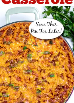 Pinterest pin with a cheeseburger casserole skillet with ground beef, gluten free rotini pasta, peppers, and onion topped with cheddar cheese and broiled, then topped with fresh parsley. There's fresh parsley on the table next to the skillet.