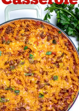 Pinterest pin with a cheeseburger casserole skillet with ground beef, gluten free rotini pasta, peppers, and onion topped with cheddar cheese and broiled, then topped with fresh parsley. There's fresh parsley on the table next to the skillet.