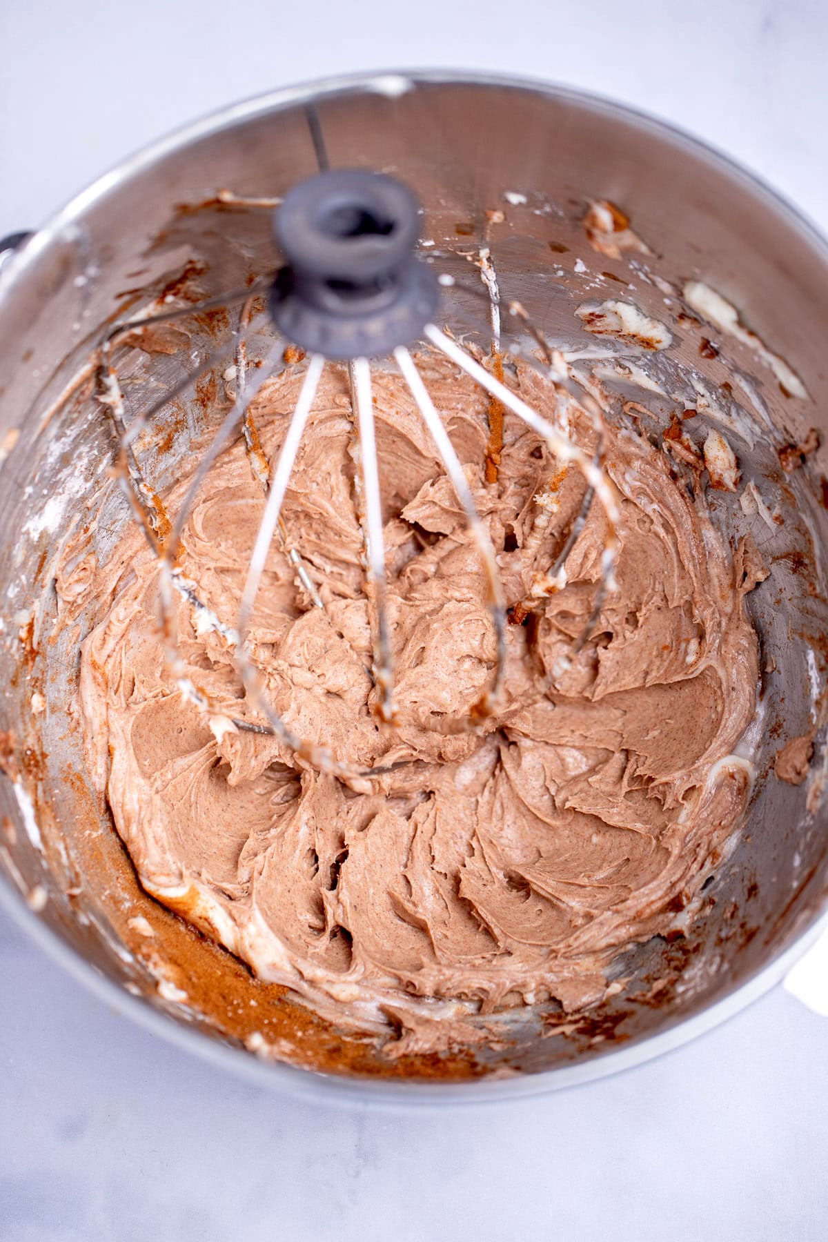 A mixing bowl with a stand mixer whisk in it, with creamed together powdered sugar, cream cheese, and pumpkin pie spice.