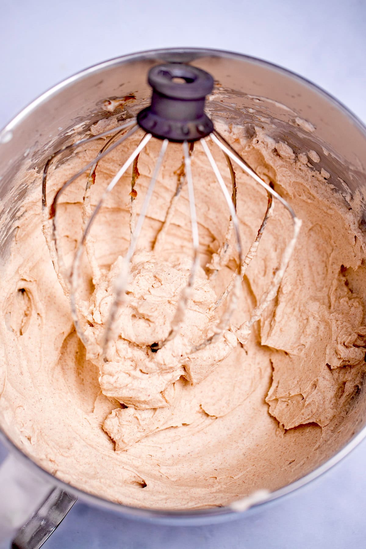 A mixing bowl with a stand mixer whisk in it with whipped pumpkin spice cream cheese in it.