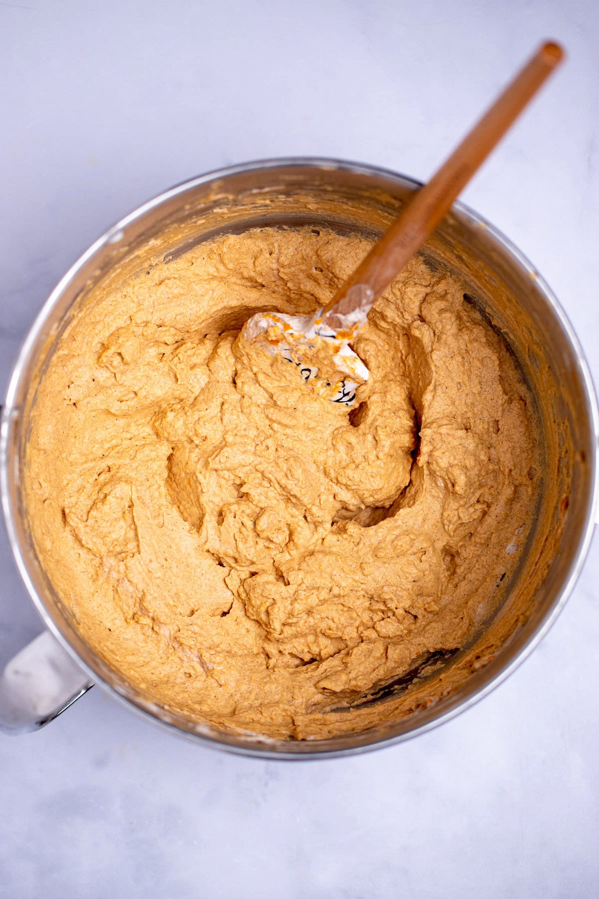 A mixing bowl with pumpkin pie dip with a spatula in it.