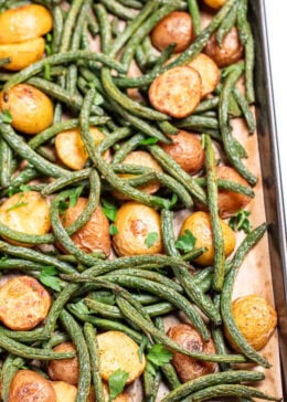 Pinterest pin with a sheet pan lined with parchment paper with roasted green beans and potatoes with olive oil and spices, topped with fresh parsley.