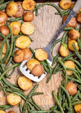 Pinterest pin with a sheet pan lined with parchment paper with roasted green beans and potatoes with olive oil and spices, topped with fresh parsley, and a spatula resting on the sheet pan.