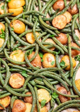 Pinterest pin with a sheet pan lined with parchment paper with roasted green beans and potatoes with olive oil and spices, topped with fresh parsley.