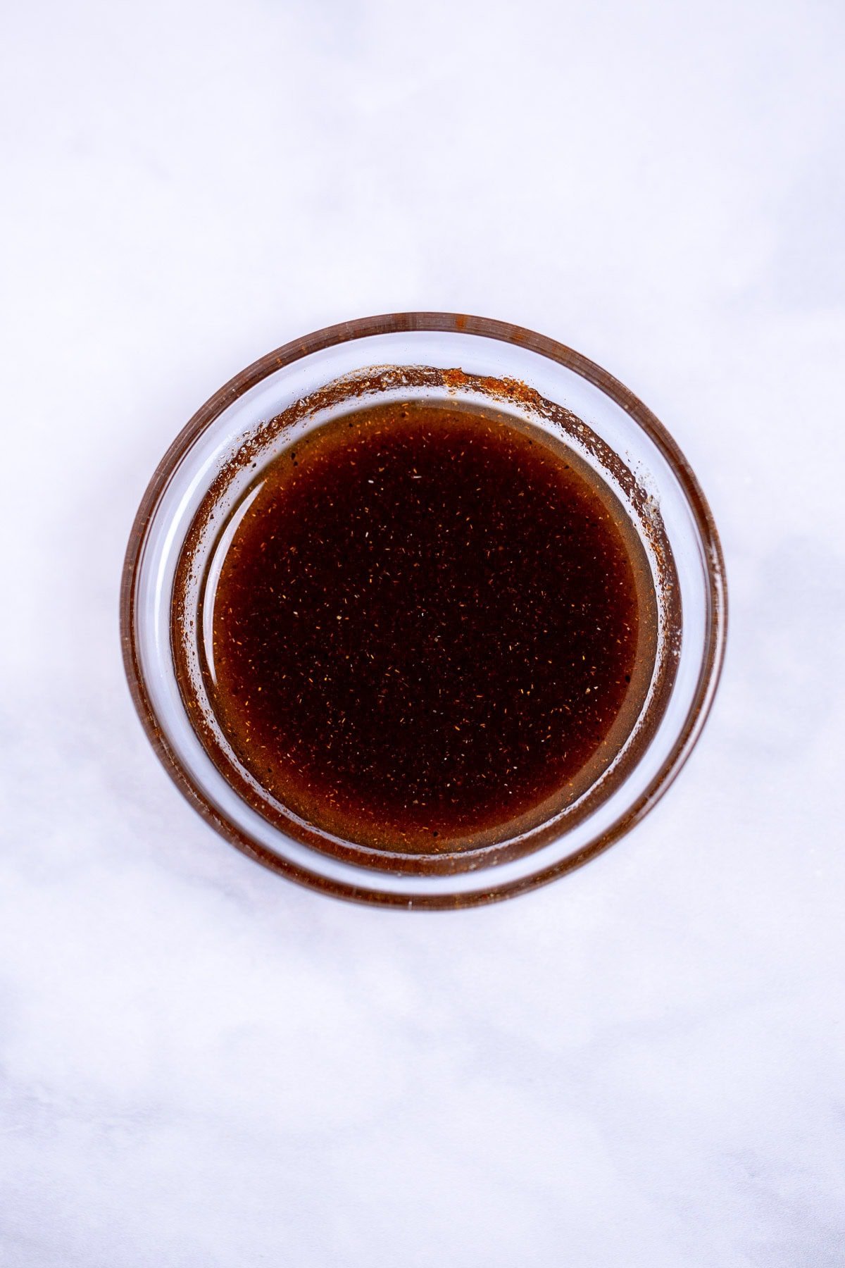 A small glass bowl with olive oil and spices mixed together.