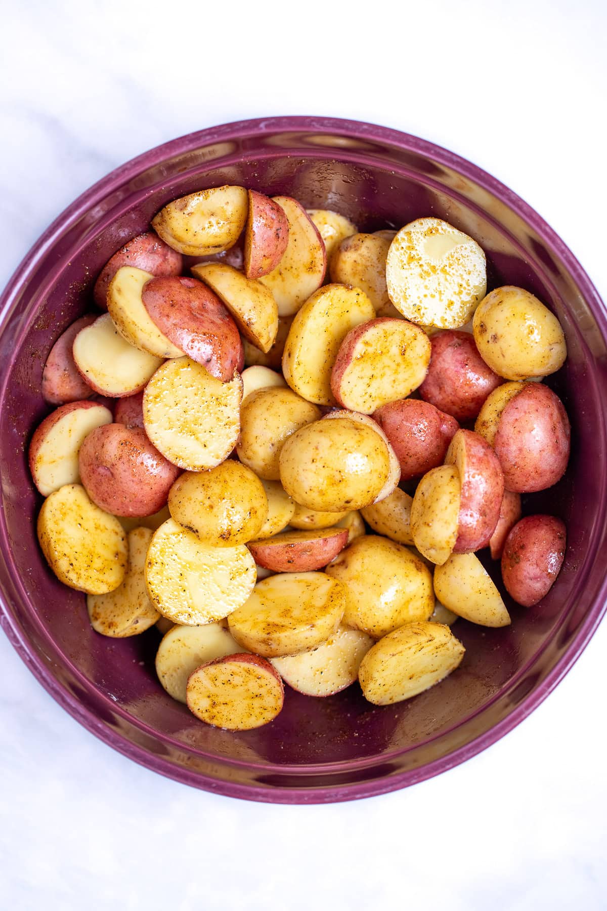 A mixing bowl with potatoes tossed with olive oil and seasoning before being cooked.