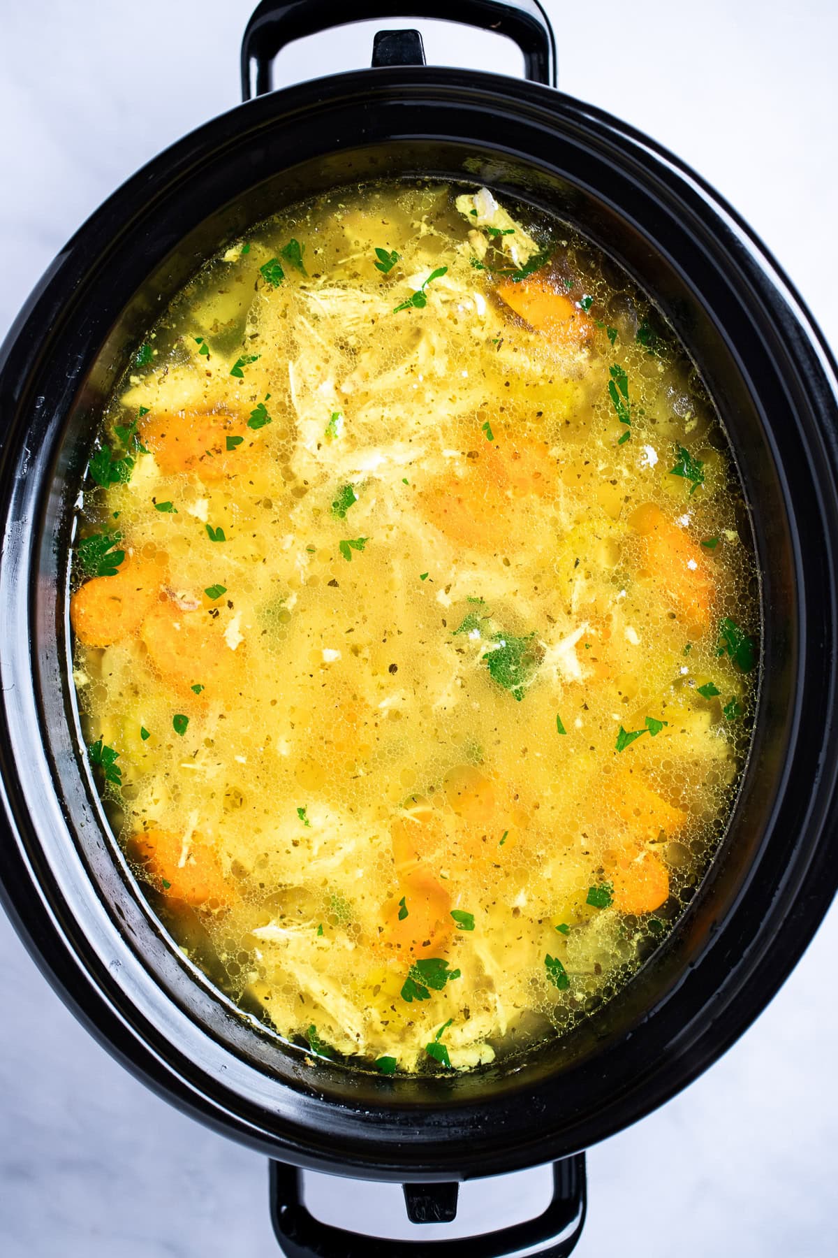 A slow cooker with chicken soup topped with fresh parsley.