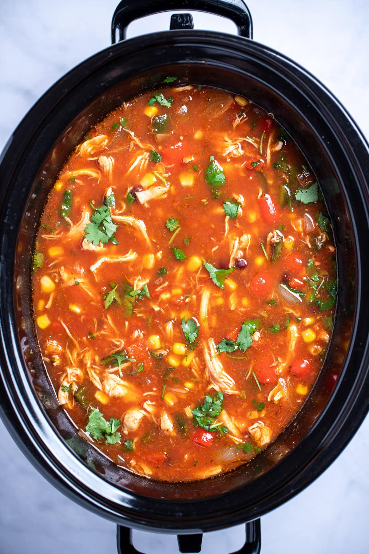 A slow cooker with chicken tortilla soup topped with fresh cilantro.