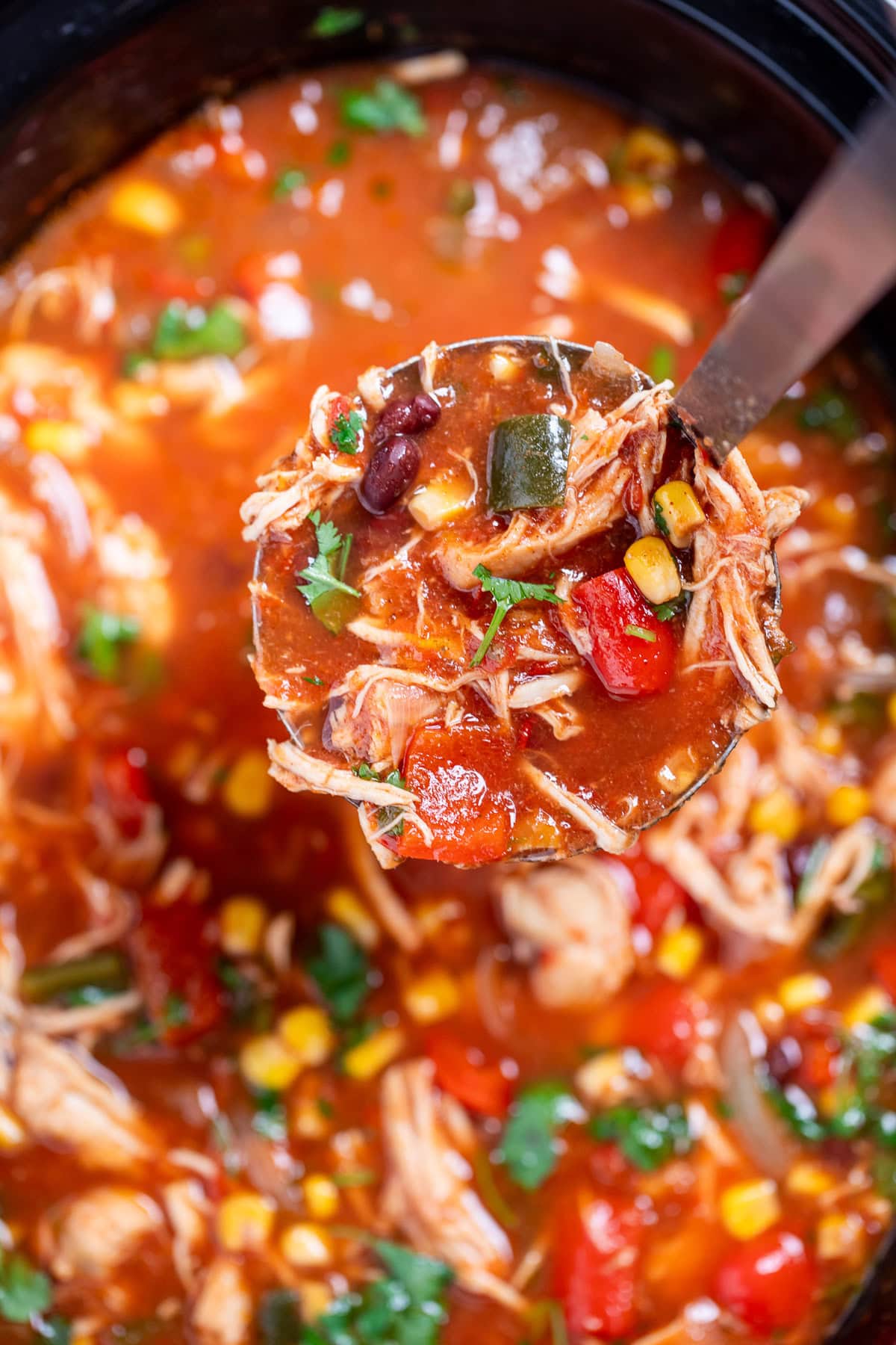 A slow cooker with chicken tortilla soup topped with fresh cilantro, with a ladle lifting some soup up.