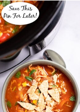Pinterest pin with a bowl of chicken tortilla soup topped with fresh cilantro and crushed tortilla chips with a spoon on the table next to it, and the crockpot behind it.