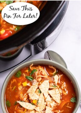 Pinterest pin with a bowl of chicken tortilla soup topped with fresh cilantro and crushed tortilla chips with a spoon on the table next to it, and the crockpot behind it.
