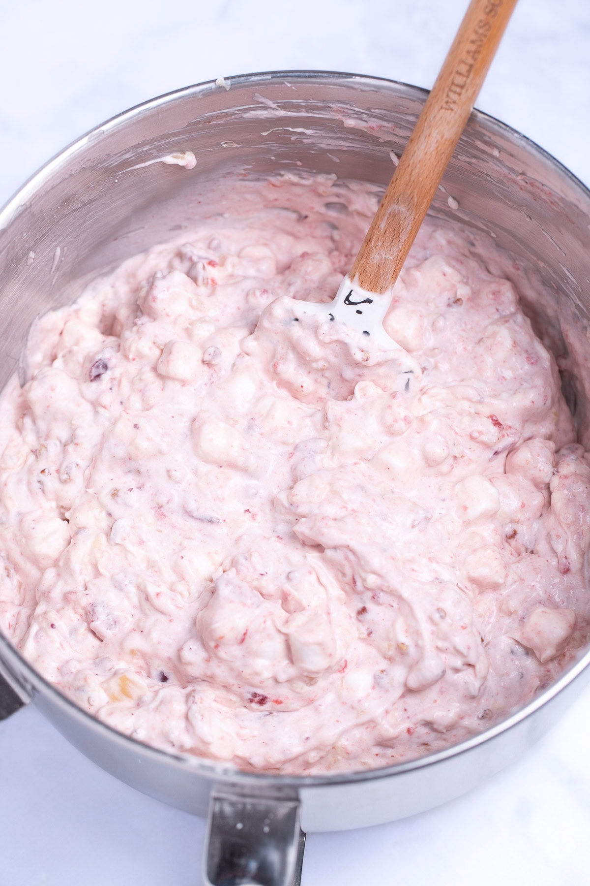 A mixing bowl with cranberry fluff salad and a spatula in it on a table.