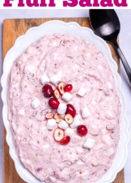 Pinterest pin with a serving bowl with cranberry fluff salad topped with mini marshmallows and fresh cranberries, resting on a cutting board, next to a cup of fresh cranberries and a serving spoon.