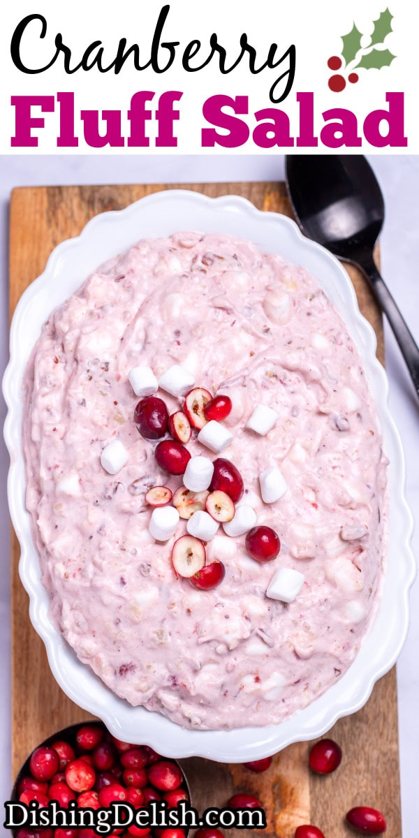 Pinterest pin with a serving bowl with cranberry fluff salad topped with mini marshmallows and fresh cranberries, resting on a cutting board, next to a cup of fresh cranberries and a serving spoon.