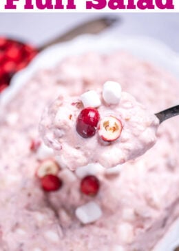 Pinterest pin with a serving bowl with cranberry fluff salad topped with mini marshmallows and fresh cranberries, resting on a cutting board, next to a cup of fresh cranberries and a serving spoon lifting some fluff up.