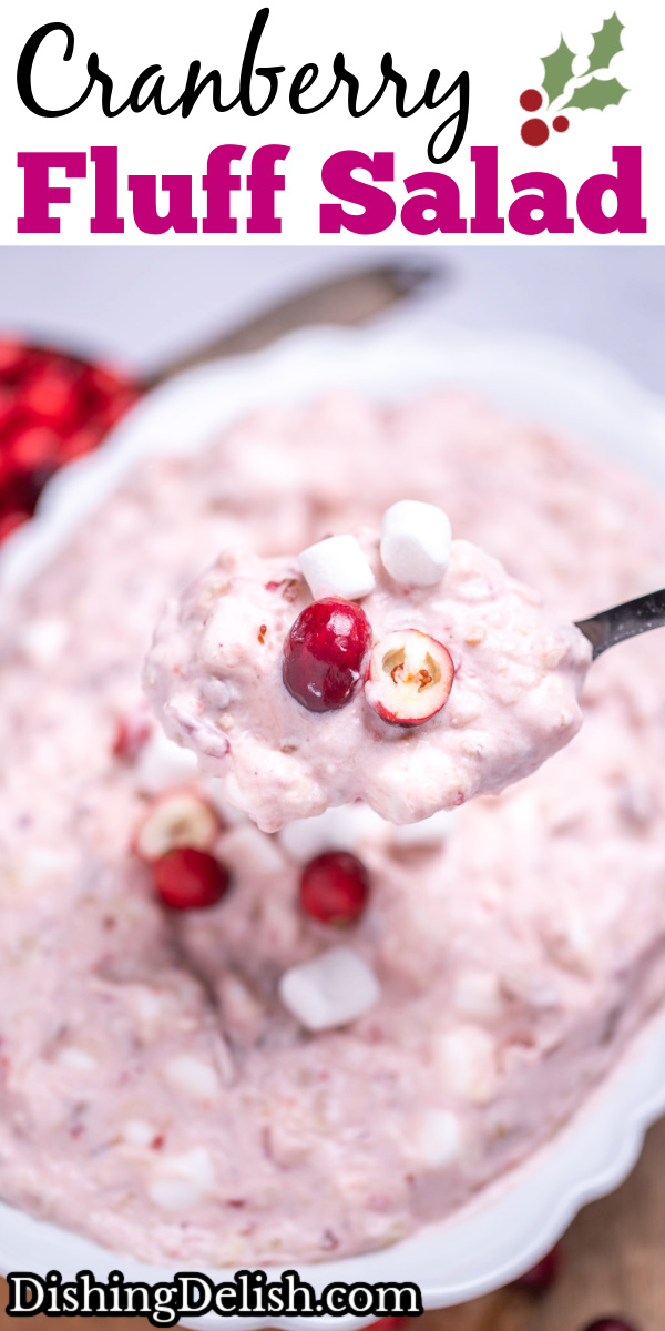 Pinterest pin with a serving bowl with cranberry fluff salad topped with mini marshmallows and fresh cranberries, resting on a cutting board, next to a cup of fresh cranberries and a serving spoon lifting some fluff up.