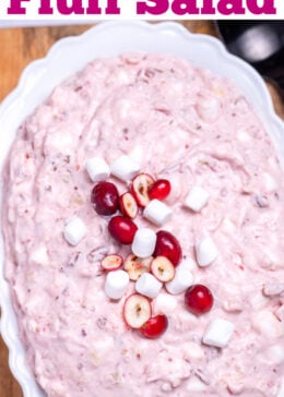 Pinterest pin with a serving bowl with cranberry fluff salad topped with mini marshmallows and fresh cranberries, resting on a cutting board, next to a cup of fresh cranberries and a serving spoon.