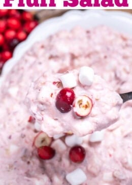 Pinterest pin with a serving bowl with cranberry fluff salad topped with mini marshmallows and fresh cranberries, resting on a cutting board, next to a cup of fresh cranberries and a serving spoon lifting some fluff up.