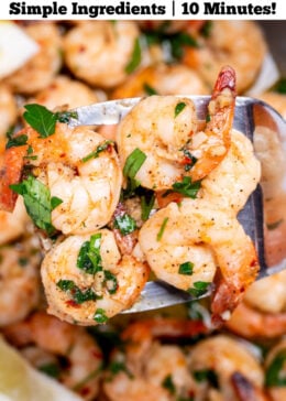 Pinterest pin with a nonstick skillet with cooked shrimp in garlic and butter with fresh parsley and two lemon wedges in the skillet, with a spatula lifting some up.