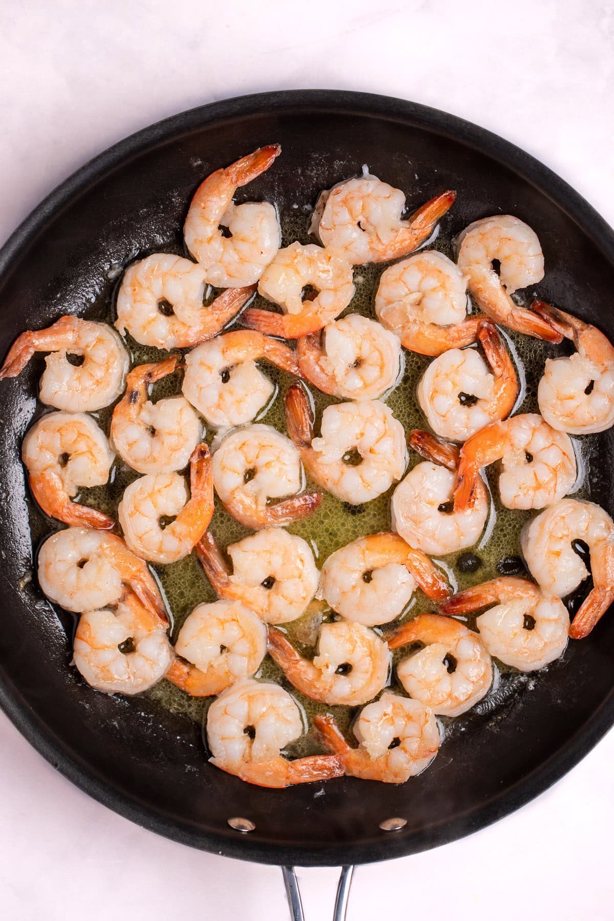 A nonstick skillet with cooked shrimp in melted butter.