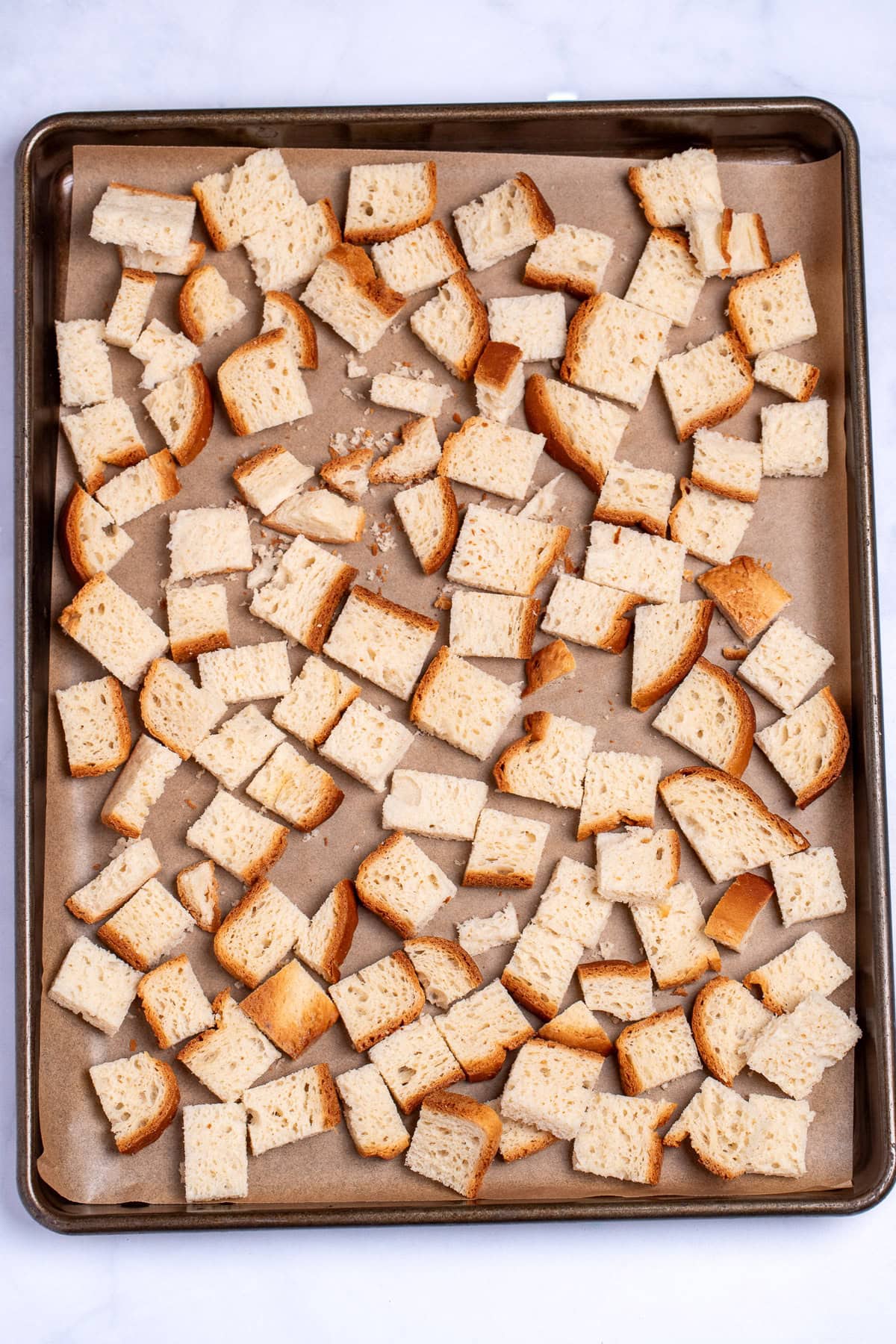 Cubes of gluten free bread on a sheet pan lined with parchment paper, before being toasted.