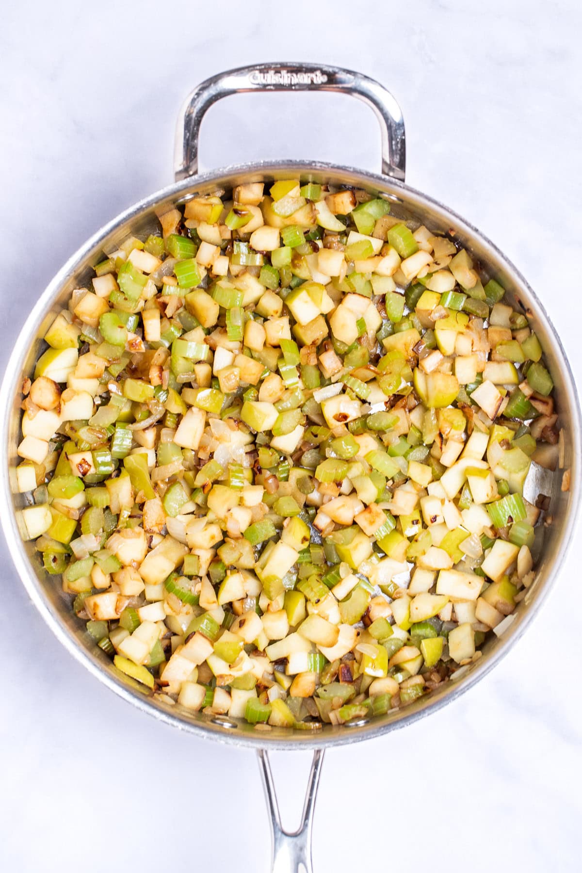 A saute pan with celery, onion, parsnips, and apple cut into small pieces and sautéed.