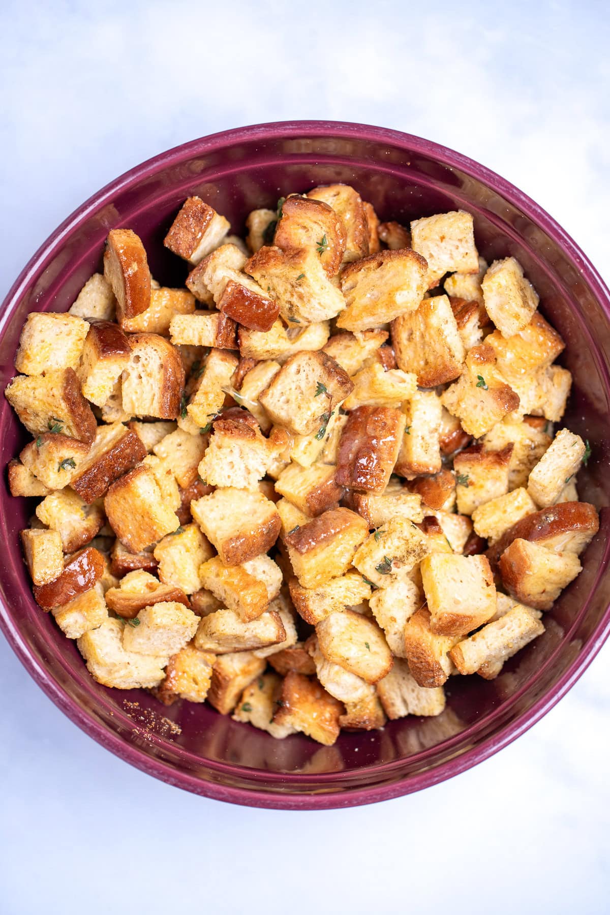 A mixing bowl with gluten free bread cubes covered in egg and seasoning before being cooked.