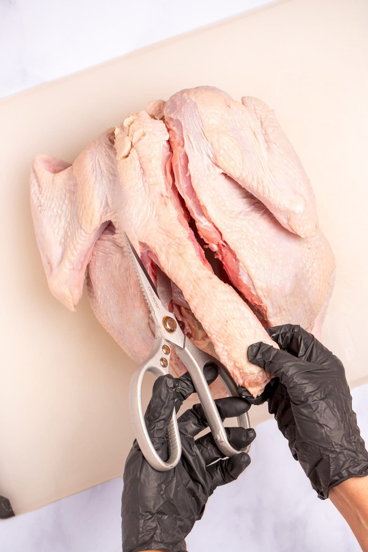 Hands cutting the spine out of a whole turkey on a cutting board.