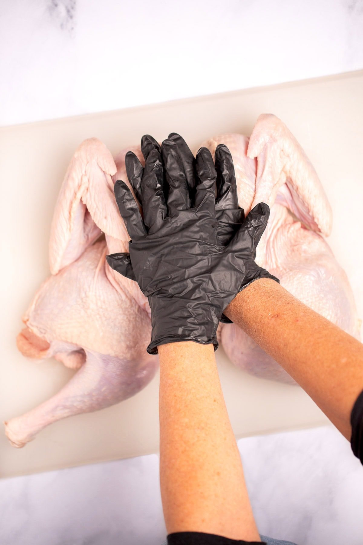 Two hands pressing down on the breast of a whole turkey on a cutting board.