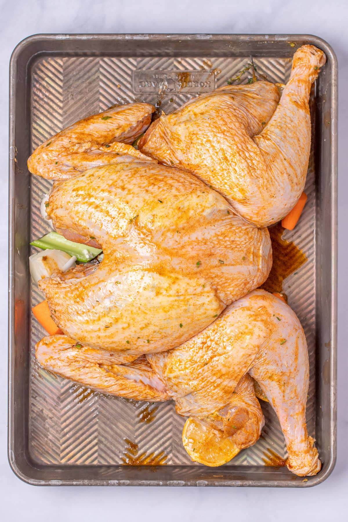 A roasting pan with a butterflied whole turkey on top of lemon and vegetables, coated in oil and seasoning, before being roasted.