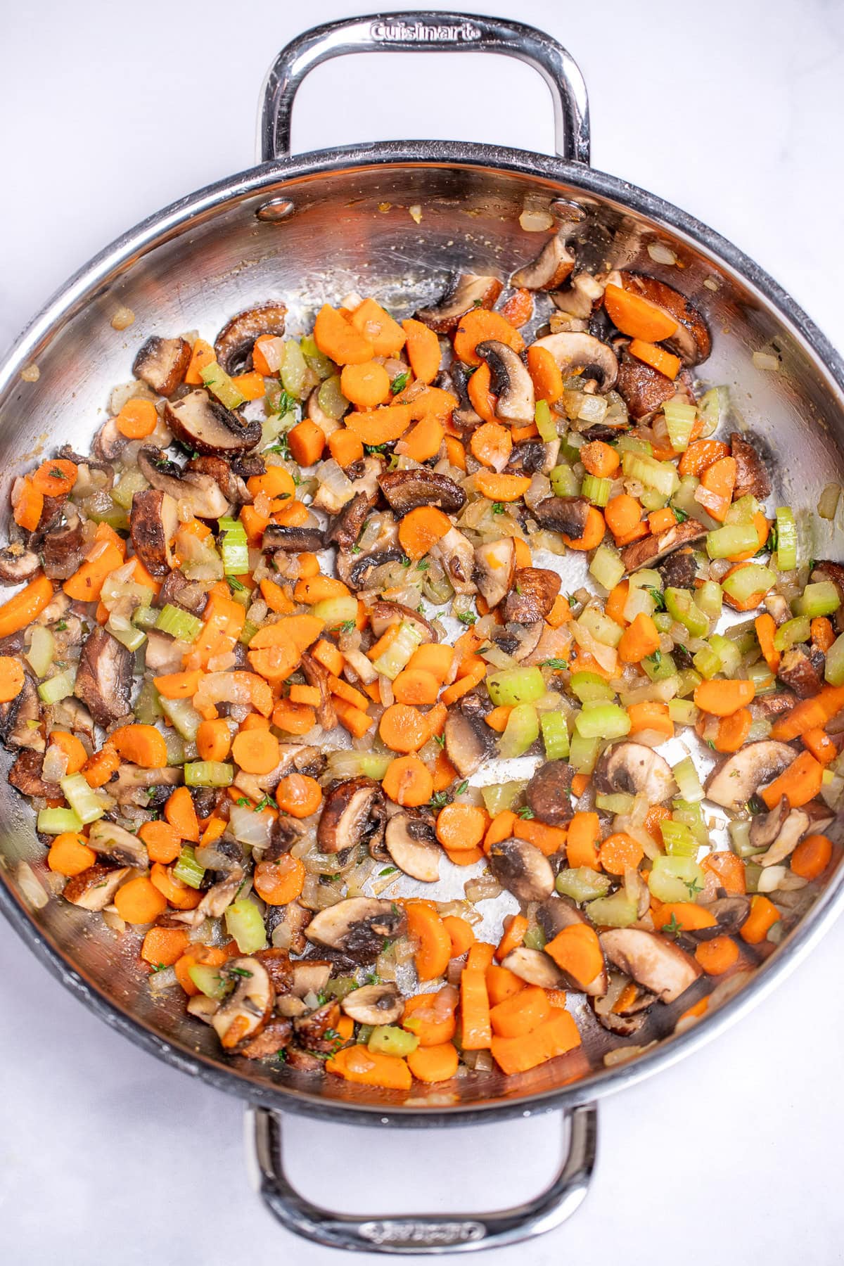 A saute pan with carrots, celery, onion, and mushrooms seasoned and cooked.