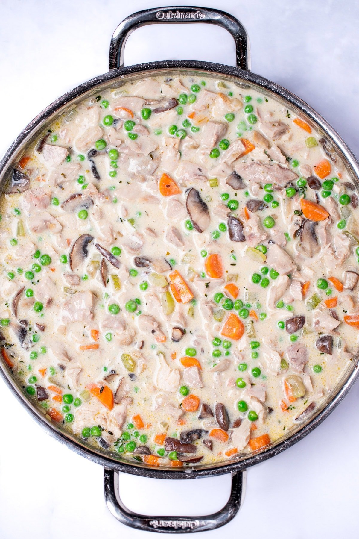 A saute pan with pot pie filling fully cooked with carrots, mushrooms, celery, peas, and onion in a creamy sauce.