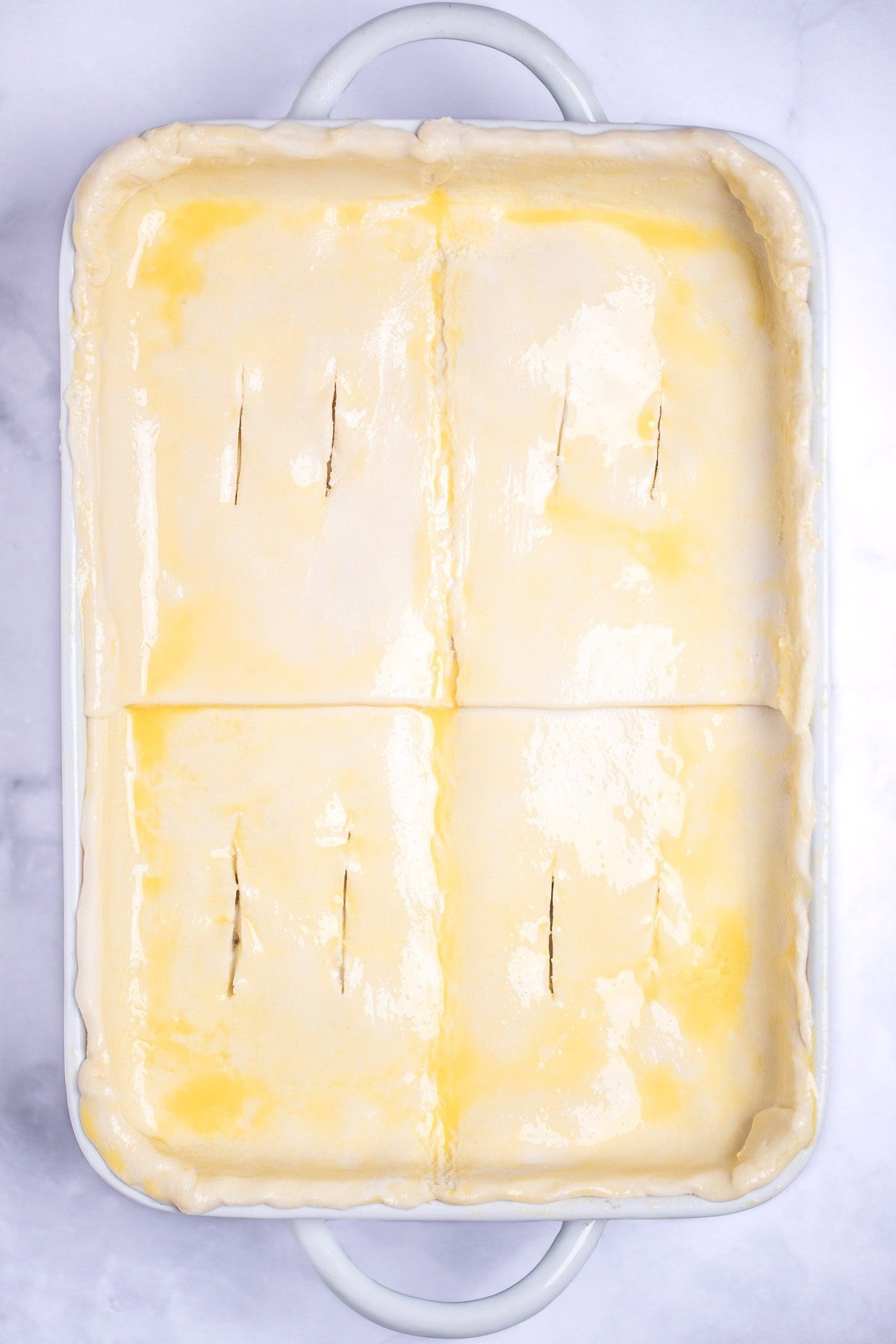 A baking dish with raw puff pastry topped with egg wash before being cooked.