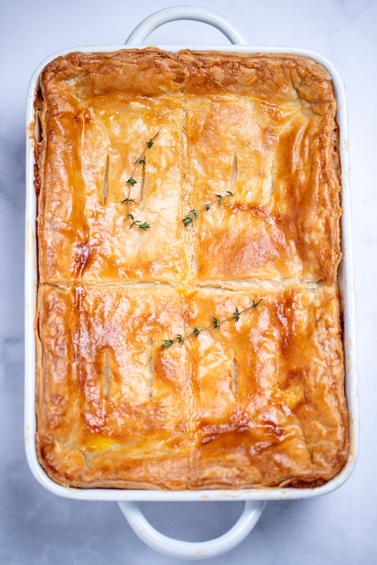 A baking dish with golden brown puff pastry on top and a sprig of thyme.