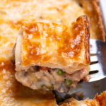 A baking dish with leftover turkey pot pie casserole with a flakey puff pastry crust, and a spatula lifting some up.