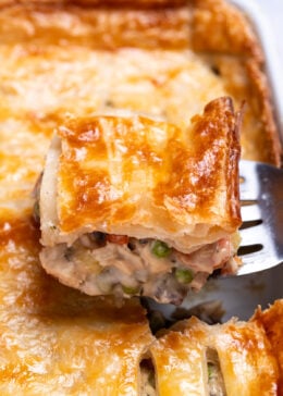 A baking dish with leftover turkey pot pie casserole with a flakey puff pastry crust, and a spatula lifting some up.