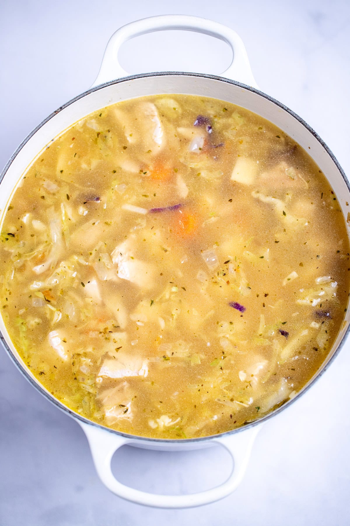 A dutch oven with broth and coleslaw mix in it before being simmered.