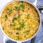A dutch oven on a table with turkey soup topped with fresh parsley, next to a towel with a ladle on it on the table.