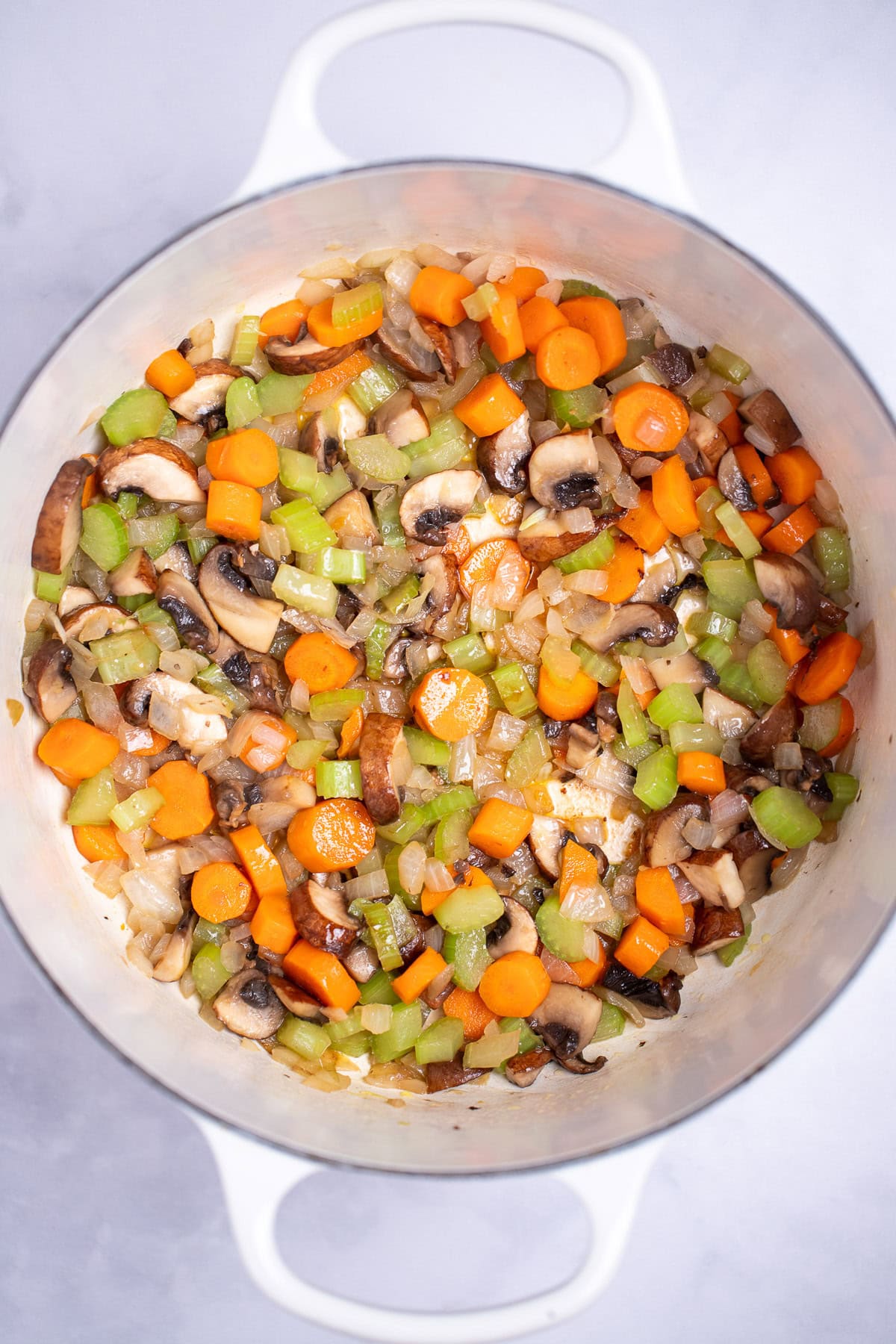 Colorful vegetable stir-fry with carrots, celery, mushrooms, and onions in a white dutch oven.