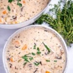 A bowl of turkey wild rice soup in front of a dutch oven of soup, with fresh thyme on the side of the bowl.