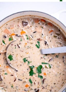Pinterest pin with delicious homemade creamy leftover turkey and wild rice soup garnished with fresh parsley in a dutch oven, with a ladle resting in the soup.