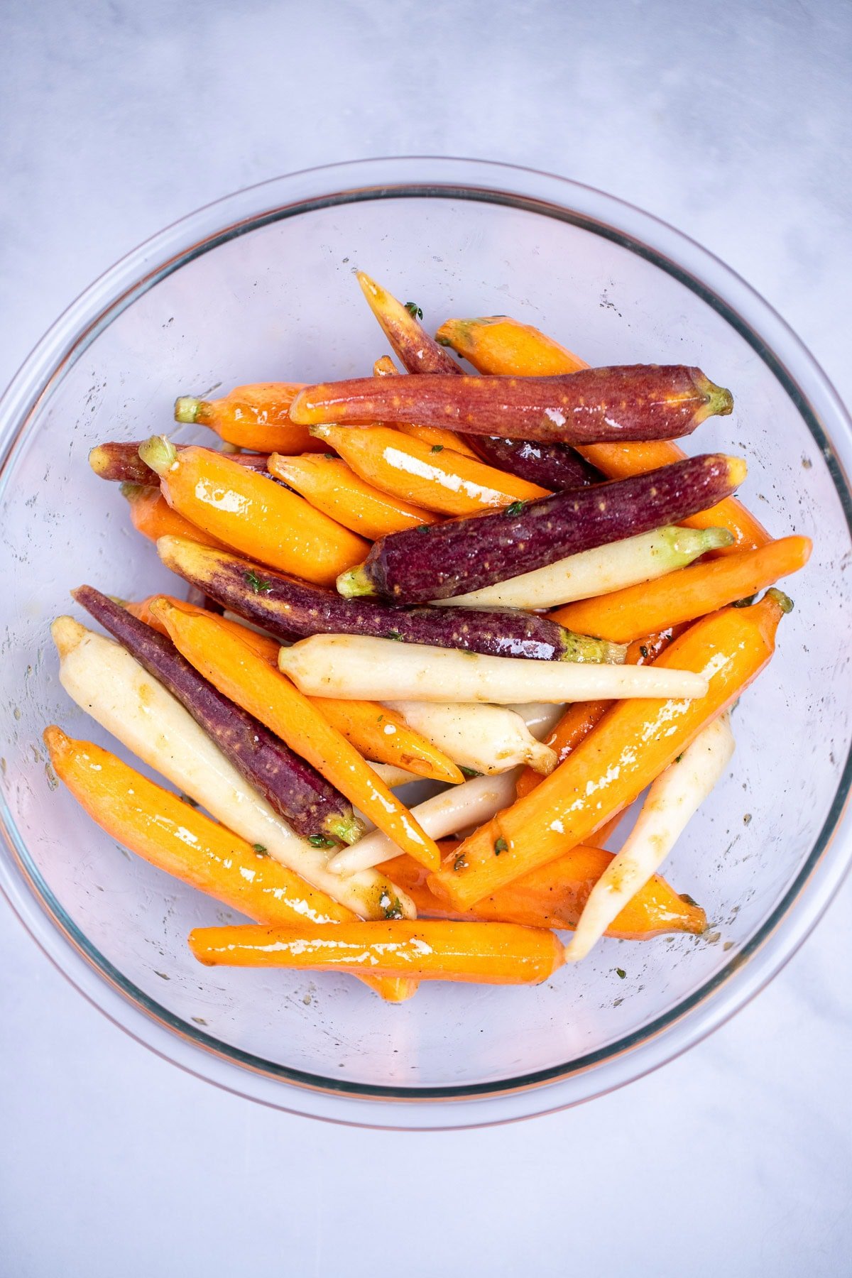 A glass bowl on a table filled with carrots tossed in spices and olive oil.