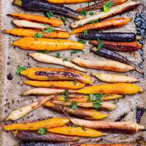 A sheet pan lined with parchment paper with roasted and caramelized rainbow carrots in a single layer, with sprigs of fresh thyme, after being roasted.