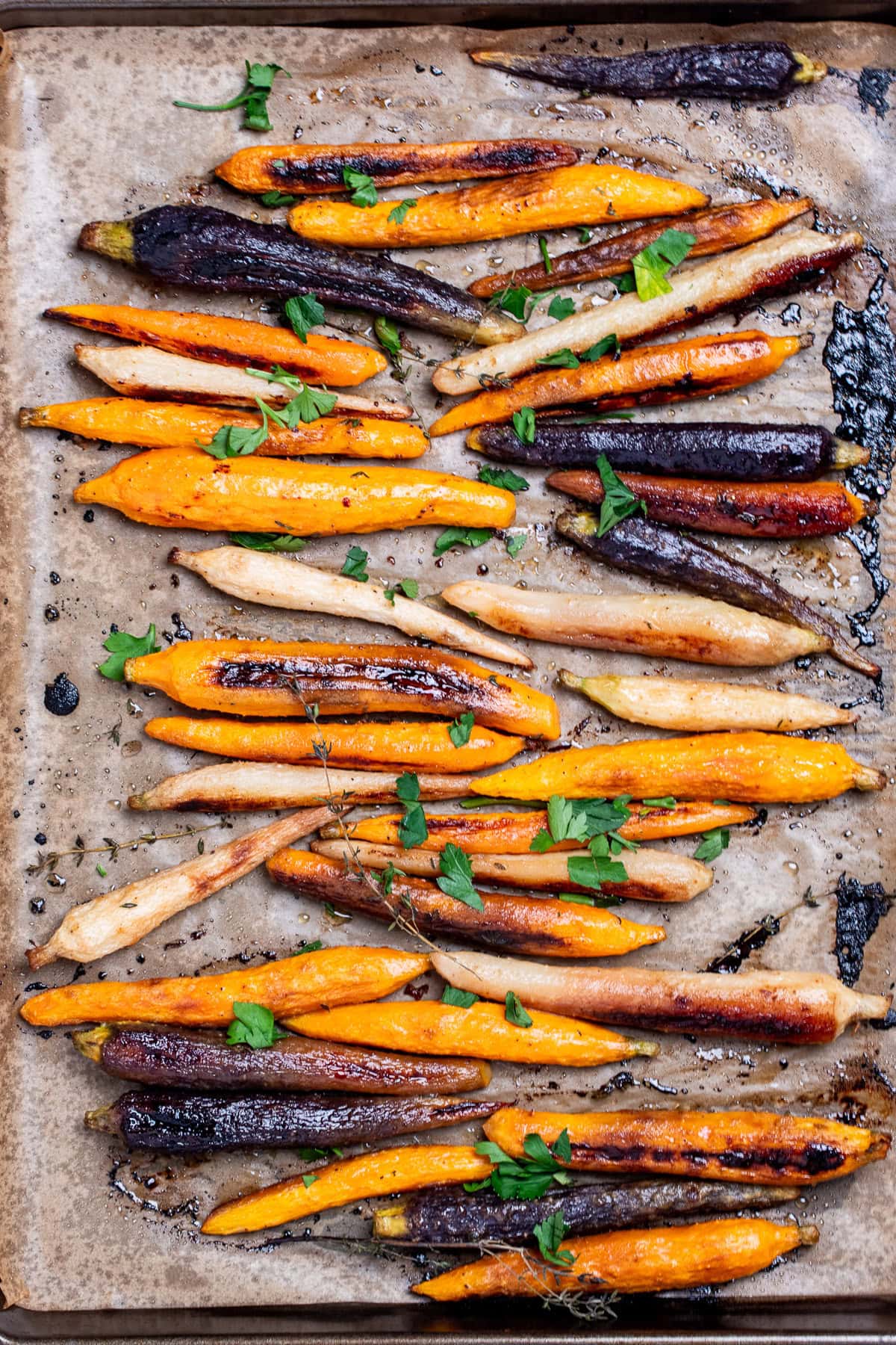 A sheet pan lined with parchment paper with roasted and caramelized rainbow carrots in a single layer, with sprigs of fresh thyme, after being roasted.