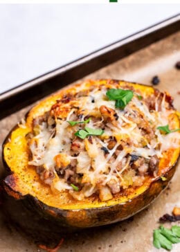 Pinterest pin with a sheet pan lined with parchment paper with halves of acorn squash stuffed with ground sausage and vegetables and topped with melted mozzarella and fresh parsley.