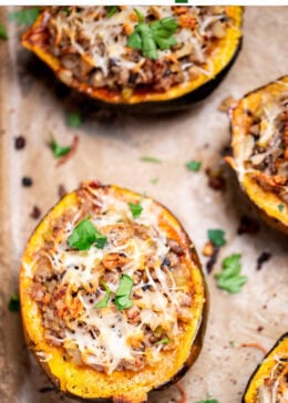 Pinterest pin with a sheet pan lined with parchment paper with halves of acorn squash stuffed with ground sausage and vegetables and topped with melted mozzarella and fresh parsley.