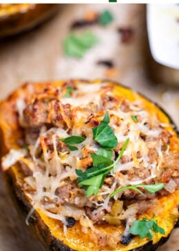 Pinterest pin with a sheet pan lined with parchment paper with halves of acorn squash stuffed with ground sausage and vegetables and topped with melted mozzarella and fresh parsley.